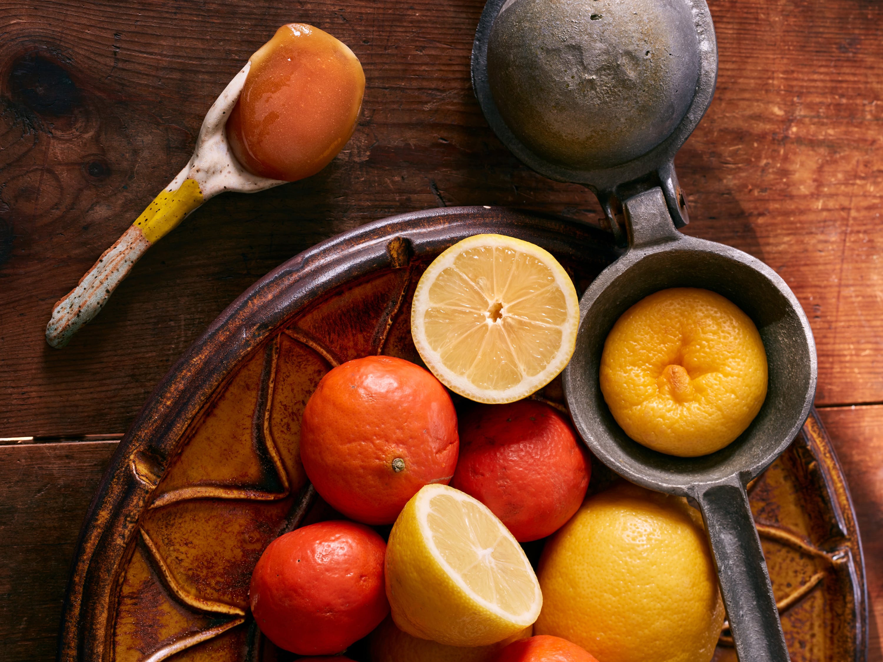 A spoonful of manuka honey sits on a table with citrus fruits.