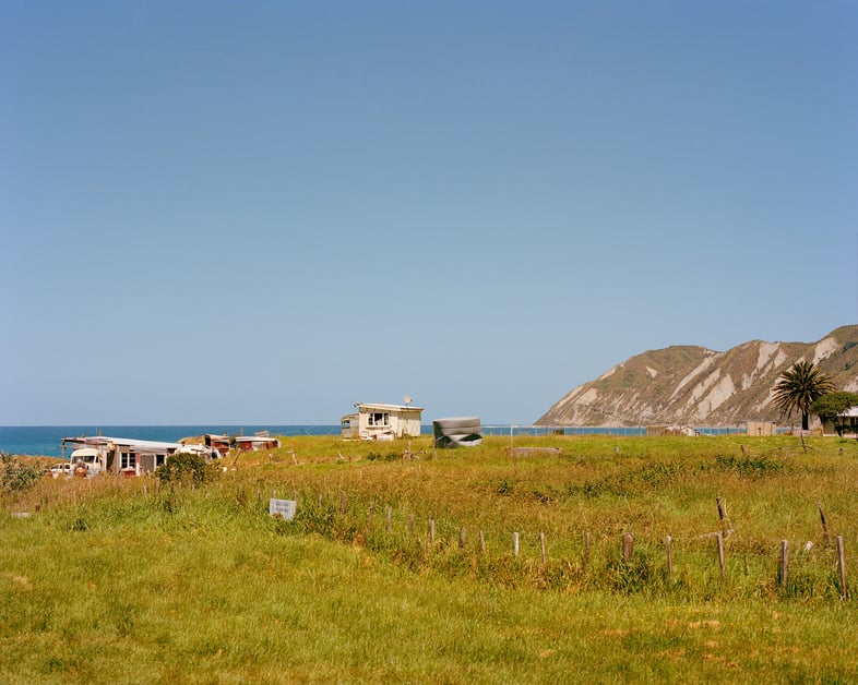 Small houses sit on a green field against the New Zealand coastline.
