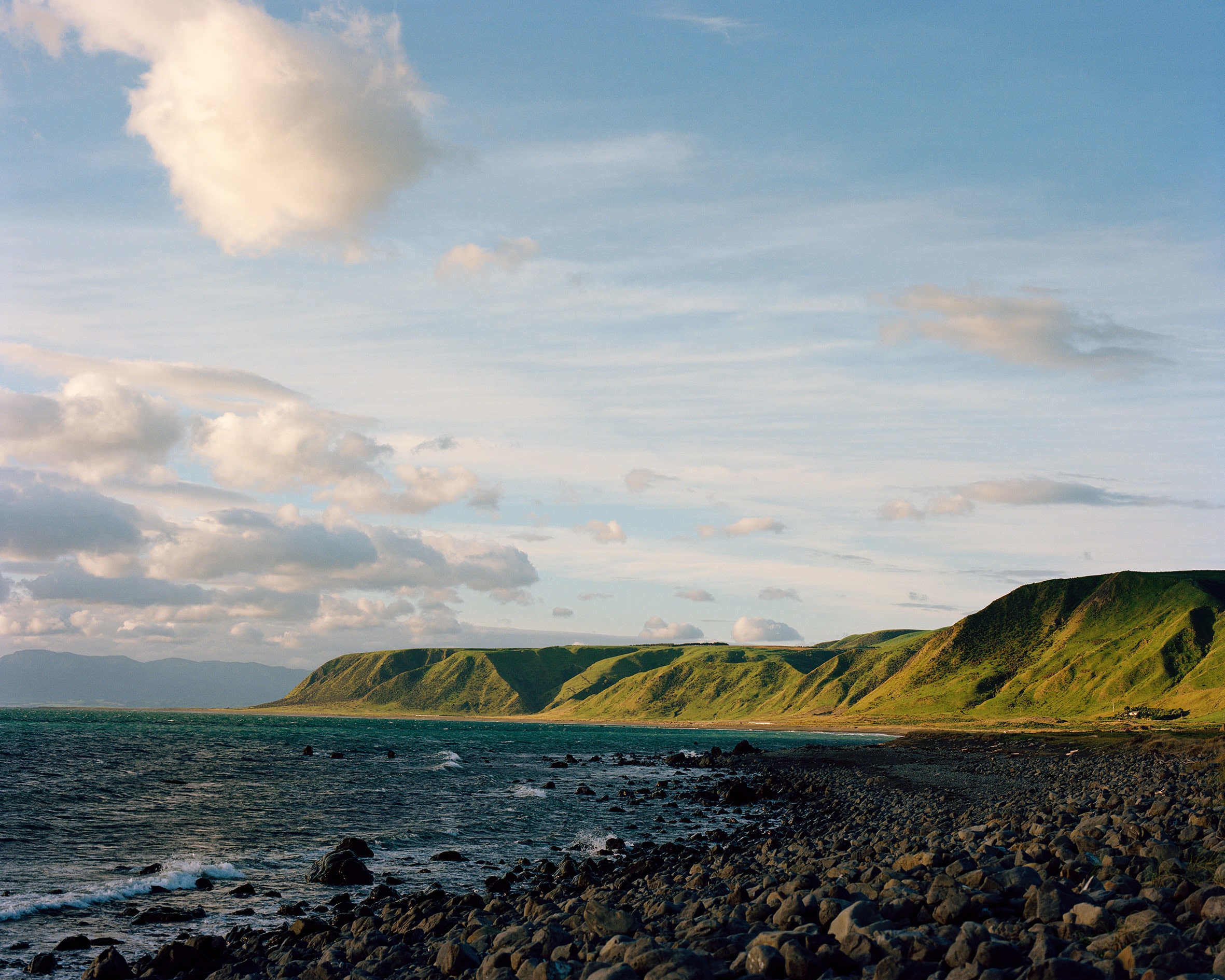 A rocky beach with green mountains in the background.