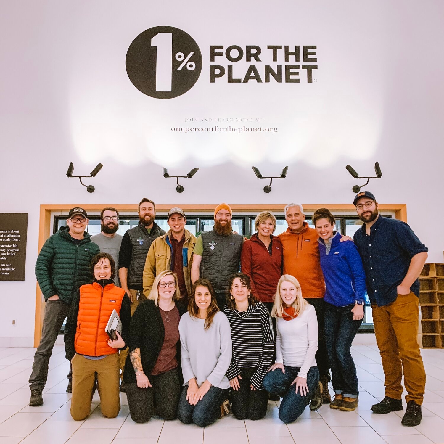 Maine Beer Company team posing for a photo under the 1% for the Planet logo on their taproom wall