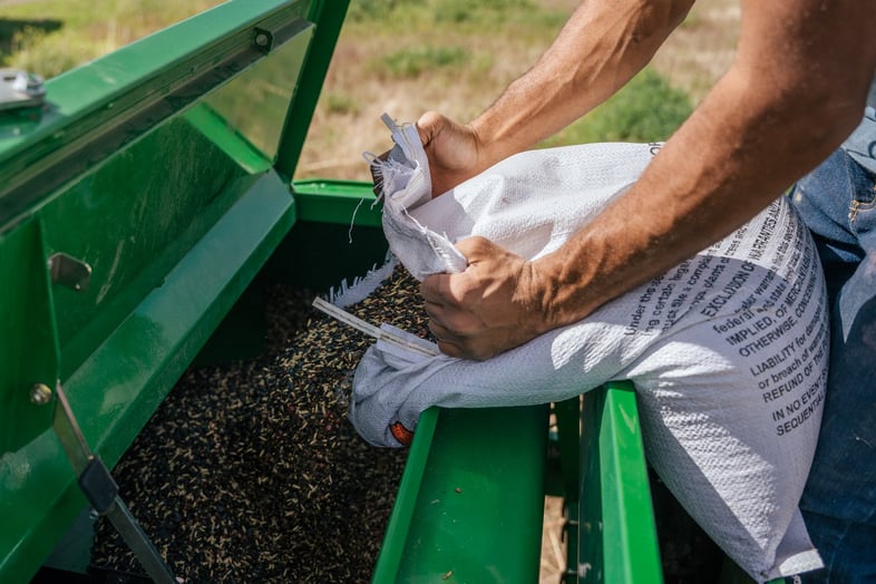 A person dumping a bag of grains into a farming machine
