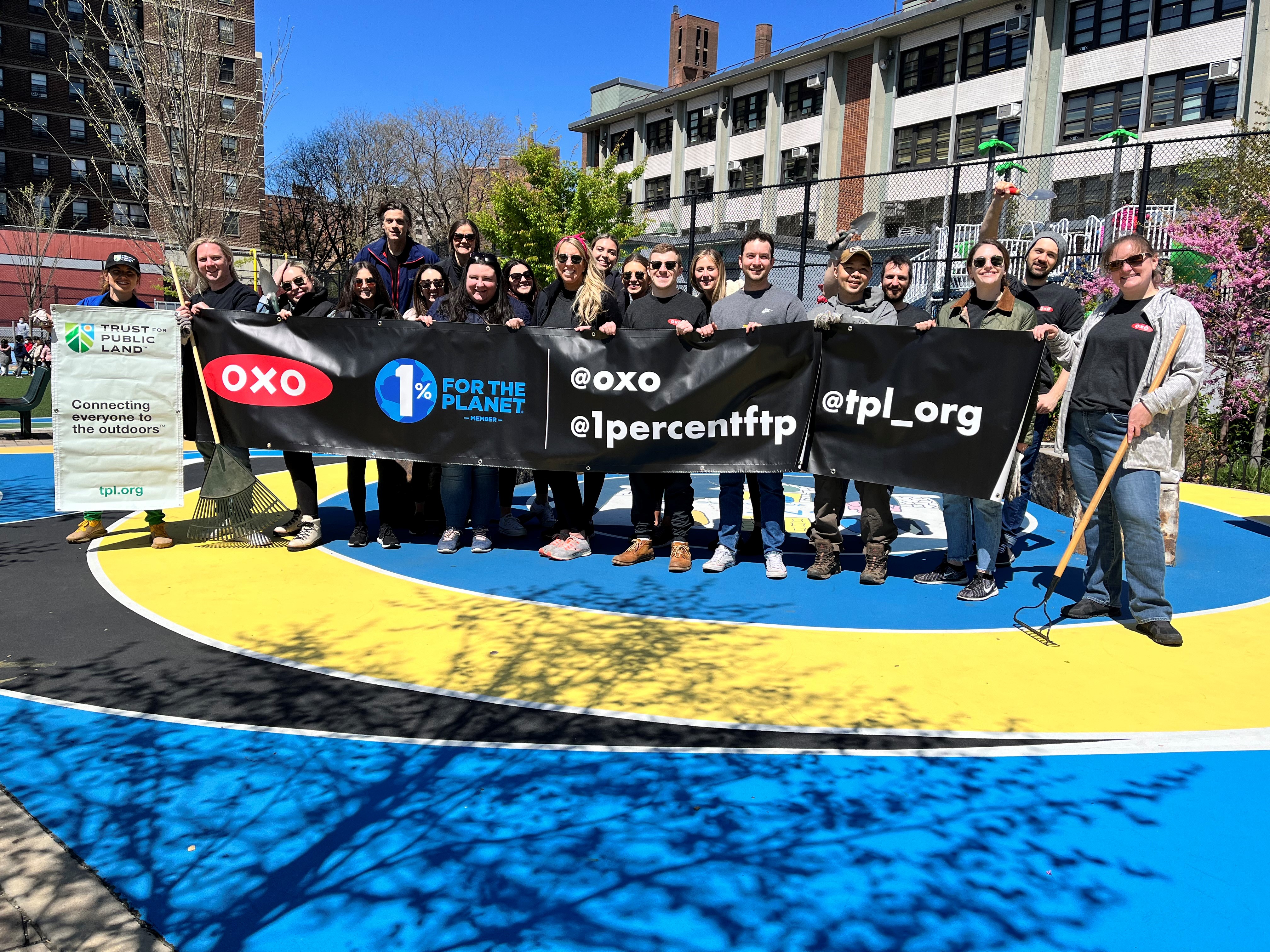 OXO and Trust for Public Lands teams holding up a banner with their logos after a corporate volunteer day. 